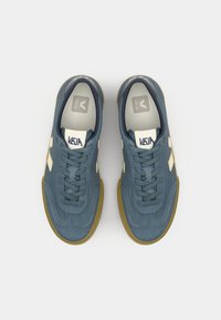 Adidași din piele întoarsă albastră cu accente albe pe laterale, dotati cu șireturi rotunde, talpă din cauciuc și branț căptușit cu un logo.