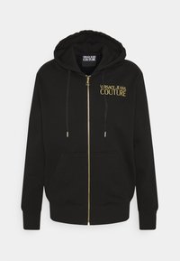 Sudadera con cremallera negra hecha de algodón, con un logo bordado en oro en el lado izquierdo del pecho y cordones. Incluye bolsillos delanteros.