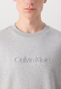 Light gray sweatshirt with a crew neckline, made of soft fabric, featuring an embroidered "Calvin Klein" logo in a slightly darker gray.