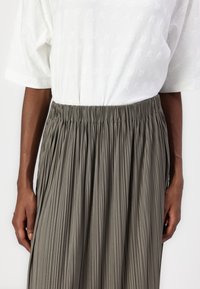Fustă plisată, de lungime medie, dintr-un material gri deschis, cu talie elastică. Partea de sus este o cămașă albă lejeră, cu un model texturat subtil.