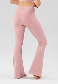 Uitlopende actieve legging in lichtroze geribbelde stof, met een brede tailleband en naadloos ontwerp voor comfort en flexibiliteit.