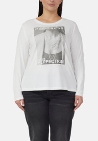Witte shirt met lange mouwen met een grafische print met de tekst "PROGRESS over PERFECTION" en een ontwerp van een gelaagde parelketting. Gemaakt van katoen, met een losse pasvorm.