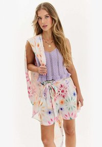Levanduľový pletený crop top, skombinovaný s mnohobarevnými tie-dye šortkami a zodpovedajúcim ľahkým kabátom. Obsahuje viazanie na páse a kvetinový vzor.