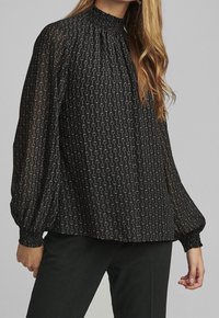 Blusa nera con collo alto arricciato, maniche a sbuffo lunghe e un delicato motivo di cerchi dorati su tutta la stoffa.