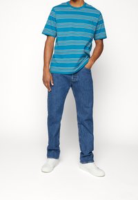 Camiseta de manga corta a rayas en color verde azulado combinada con jeans de mezclilla azul. El conjunto se completa con zapatillas blancas. La tela parece suave y casual.