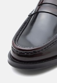 Mocassins en cuir noir à finition brillante, dotés d'un bout surpiqué, d'une bande accentuée sur le pont, et d'une semelle basse texturée.