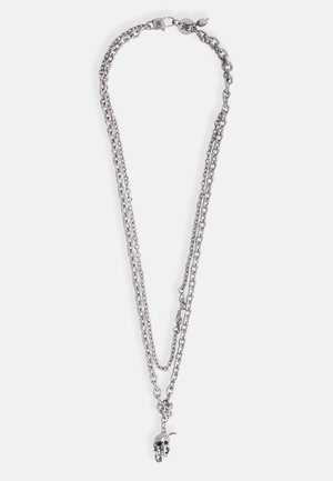 Collier en chaîne en métal argenté à plusieurs brins, finition texturée, avec un pendentif en forme de skull suspendu au centre. Détail de fermeture à clip inclus.