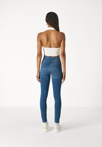 Jeans ajustados azules de denim con una cintura alta, que cuentan con bolsillos traseros y un acabado limpio. Combinados con una blusa blanca corta.