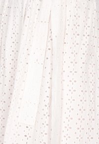 Tissu en coton blanc avec des motifs brodés en œillets. Présente des designs floraux texturés et des plis verticaux ; léger et respirant.
