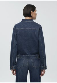 Denim jacket, dark blue color, classic collar, buttoned cuffs, and adjustable waist. Features visible stitching and back yoke detail.