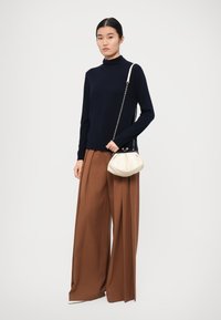 Navy turtleneck sweater, brown wide-leg pants, and a small cream handbag with a chain strap. Soft textures and contrasting colors.