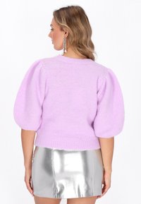 Lila gestrickter Pullover mit Puffärmeln, strukturiertem Finish und geripptem Saum. Getragen mit einem glänzenden silbernen Minirock, der eine moderne Silhouette betont.