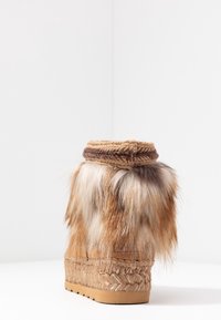 Mellanhög vinterstövel med flätad sula, mockabas och blandad brun- och vit päls runt ankeln, visad mot vit bakgrund.