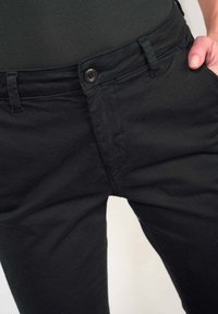 Zwarte broek van zachte stof met een sluiting aan de voorkant met knoop, riemlussen en een slim-fit ontwerp. De textuur is glad met minimale stiksels.