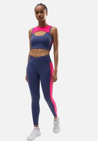 Conjunto de sujetador deportivo y leggings en azul marino con acentos en rosa; el sujetador presenta un detalle corte, los leggings tienen una textura suave y una cinturilla alta.