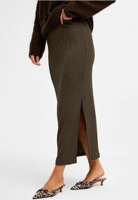 Olivgrön ribbad midi kjol med sidoklyfta, tillverkad av strukturerad tyg. Matchas med spetsiga djurmönstrade slip-on skor.