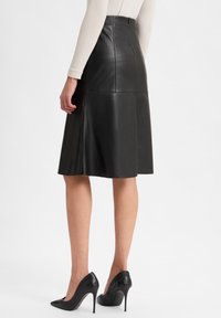 Zwarte leren rok met een flair-design, knielang, met een naadloze afwerking en zichtbare stiksels aan de achterkant. Gemaakt met zwarte hoge hakken.