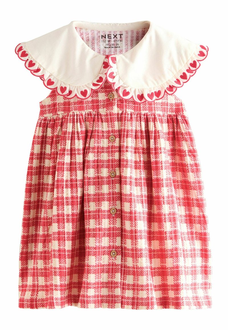 Rochie în carouri roșii și albe cu un guler alb ce are contururi de inimă, nasturi pe față și talie strânsă. Fabricată din bumbac.