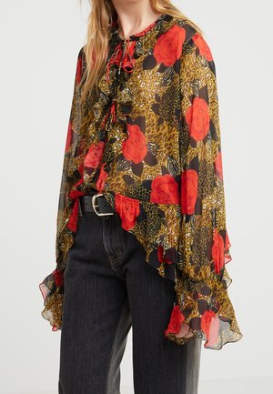 Kobieta w przezroczystej bluzce z falbankami, czerwonymi różami i wzorem w panterkę, połączona z ciemnymi dżinsami i czarnym paskiem z srebrną klamrą.