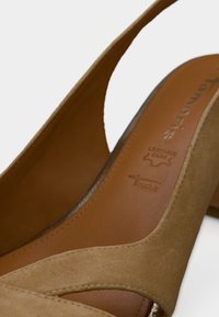 Μπεζ δερμάτινο πέδιλο με ψηλό τακούνι και σχεδιασμό με κοψίματα, με απαλή υφή. Διαθέτει καφέ εσωτερική σόλα με ανάγλυφο λογότυπο.