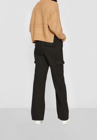 Gruby beżowy sweter o luźnym kroju, połączony z czarnymi spodniami cargo z bocznymi kieszeniami. Proste białe obuwie dopełnia całość.