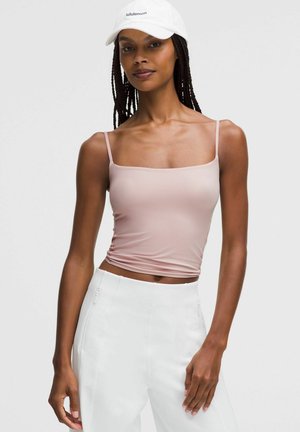 Top de tirantes finos en rosa claro, ajustado al cuerpo; textura suave. Combinado con pantalones blancos de tiro alto con bolsillos con cremallera.