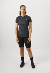 Sorte idretts T-skjorte med korte ermer, med en teksturert design og logo. Kombinert med sorte sykkelshorts og høye sneakers.