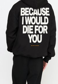 Sudadera negra con capucha con un gran texto blanco en la parte trasera que dice "PORQUE MORIRÍA POR TI" y un logo pequeño naranja "MULTIPLY APPAREL" en la parte inferior.