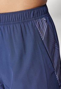 Navy athletic shorts with an elastic waistband, featuring a side pocket with a diagonal striped pattern in lighter shades. Smooth texture.