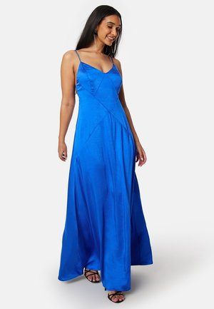 Abito maxi in satin blu con sottili spalline, corpino aderente e gonna fluida. Presenta dettagli di cuciture diagonali per dare forma.