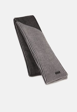 Écharpe en maille pliée avec des rayures verticales étroites noires et grises, passant du gris au noir à une extrémité, sur un fond blanc.