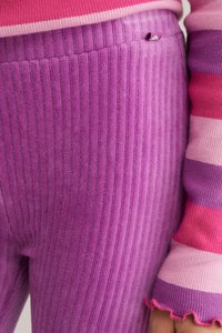 Violetti ribbed leggings on pehmeä, teksturoitu kangas. Vyötäröllä on näkyvissä pieni vaaleanpunainen yksityiskohta. Hihan reuna on monivärisiä raitoja, joissa on röyhelö.