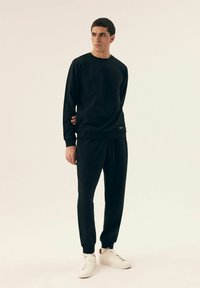 Czarny bluz z długim rękawem i dresy wykonane z miękkiego materiału. Okrągły dekolt, długie rękawy i elastyczne ściągacze. Białe sneakersy o minimalistycznym designie.