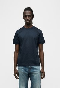 Κοντομάνικη μπλούζα σε ναυτικό μπλε με διακριτικό γεωμετρικό σχέδιο, στρογγυλή λαιμόκοψη και χαλαρή εφαρμογή, συνδυασμένη με ανοιχτόχρωμο τζιν.