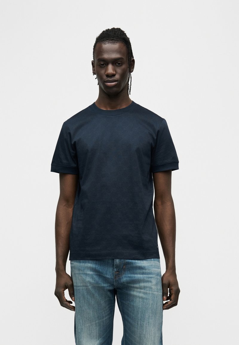 Κοντομάνικη μπλούζα σε ναυτικό μπλε με διακριτικό γεωμετρικό σχέδιο, στρογγυλή λαιμόκοψη και χαλαρή εφαρμογή, συνδυασμένη με ανοιχτόχρωμο τζιν.