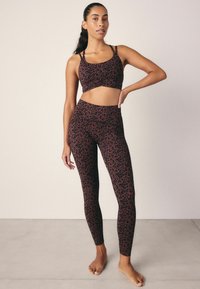 Ensemble de brassière de sport et leggings à imprimé léopard marron. Conception élastique et ajustée avec des fines bretelles, une texture lisse et une ceinture haute sur les leggings.