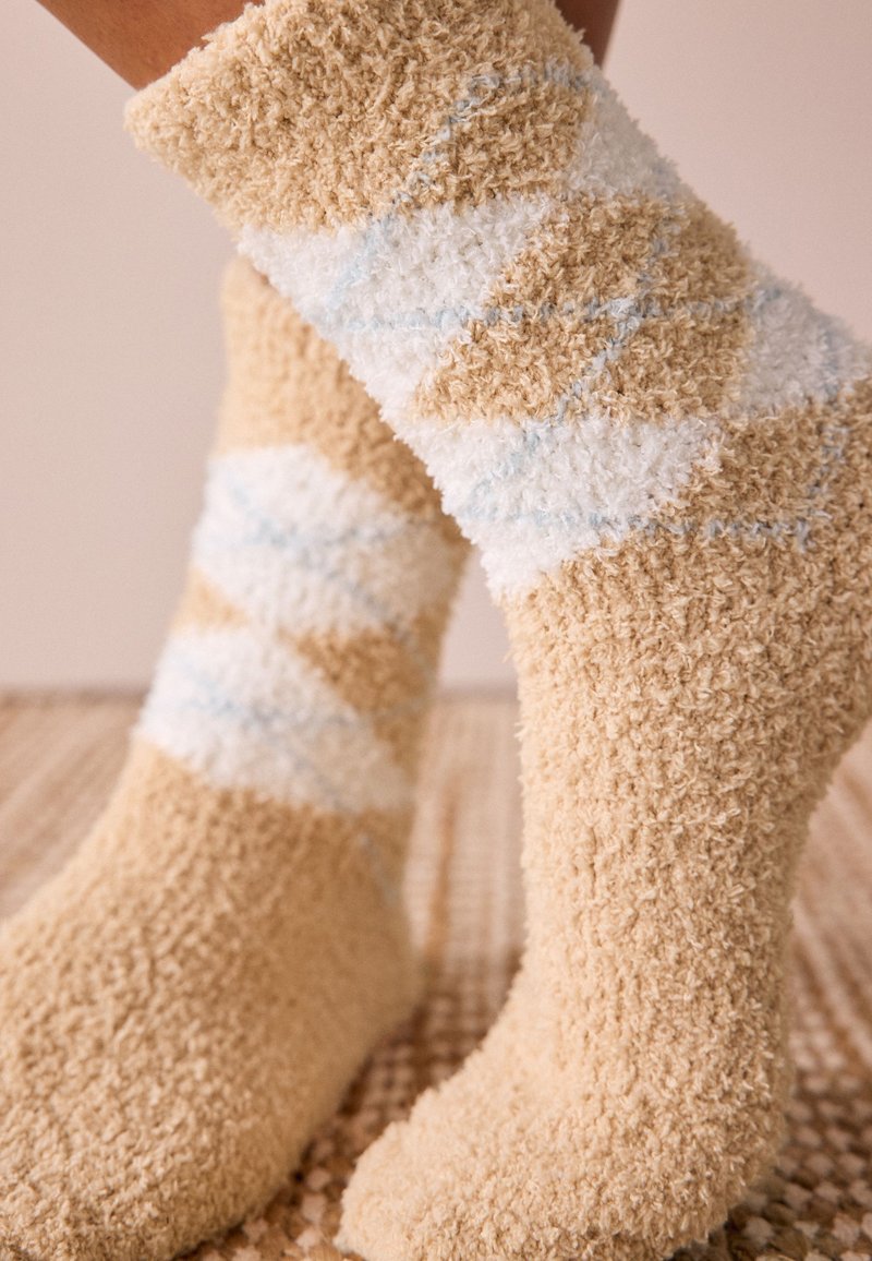 Fuzzy beige socks featuring a diagonal white and light blue striped pattern. Soft texture and cozy design suitable for indoor wear.