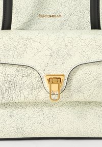 Sac à main en simili cuir crème texturé avec accents noirs, quincaillerie dorée et un fermoir triangulaire distinctif ; orné d'une finition craquelée.