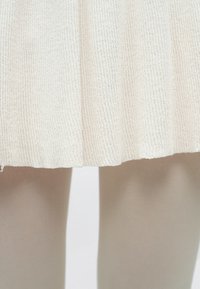 Fustă tricotată crem cu dungi, croială dreaptă, cu o suprafață texturată, asortată cu ciorapi opaci de culoare bej deschis.