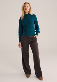 Teal knit sweater with a textured pattern, ribbed cuffs and hem, paired with wide-leg dark brown trousers and brown slip-on shoes.