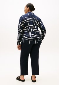 Μπλε πουκάμισο με κουμπιά με λευκές αφηρημένες ρίγες, συνδυασμένο με σκούρα παντελόνια και μαύρα παπούτσια χωρίς κορδόνια. Λείο ύφασμα, μακριά μανίκια με μανσέτες.