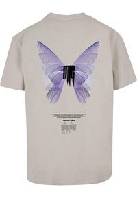 Beige Baumwoll-T-Shirt mit einem großen lila Schmetterlingsgrafik auf der Rückseite, darunter stilisierte Schrift und zusätzlich kleinere Schrift darunter.