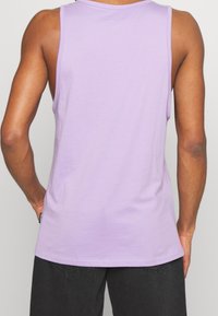 Lila linne, ärmlös design, rund halsringning, mjukt bomullstyg, slät textur, avslappnad stil, med en etikett på sidan.