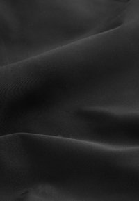 Črna tkanina z gladko, mat teksturo, ki vključuje rahle valove in gube, kar poudarja njeno lahkotnost in elastičnost.