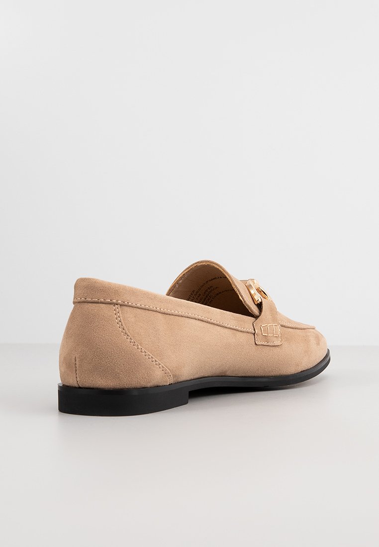 Beige Wildleder Herrenloafers mit schwarzer Sohle und goldener Metallschnalle, von der Seite auf einer schlichten weißen Fläche und Hintergrund gezeigt.