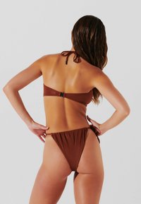Bikini marrone con coppe a triangolo e spalline regolabili. Parte bassa a vita bassa con lati arricciati, realizzata in un materiale liscio e lucido.