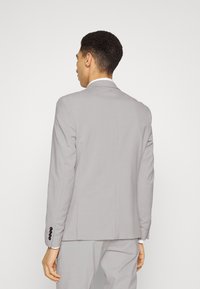 Blazer grigio con una vestibilità su misura, apertura singola sul retro e quattro bottoni neri sui polsini, realizzato in un tessuto leggero e liscio.