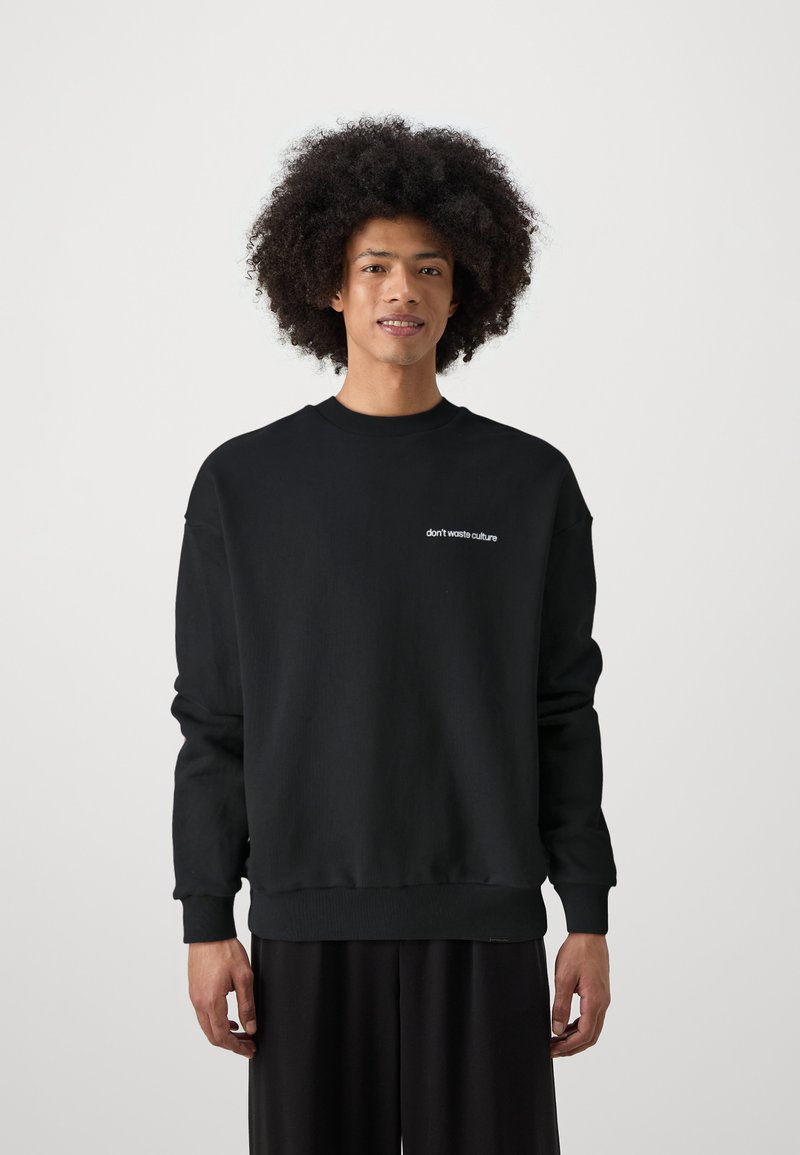 Schwarzer Pullover mit gerippten Bündchen und Saum. Auf der Vorderseite befindet sich der Text "don't waste culture" in Weiß. Hergestellt aus weichem, strapazierfähigem Stoff.