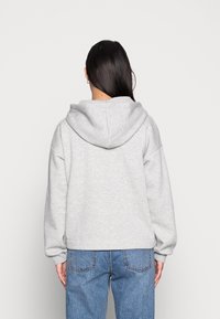 Világosszürke, oversized kapucnis pulóver, nagy kapucnival, bordázott mandzsettákkal és texturált felülettel, kék farmerral viselve, hátulról nézve.