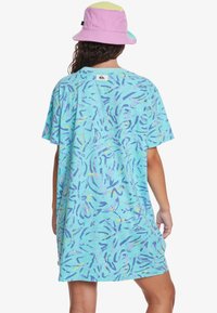 Robe T-shirt à manches courtes surdimensionnée en bleu clair avec des motifs abstraits multicolores. Le modèle porte un chapeau de seau pastel.